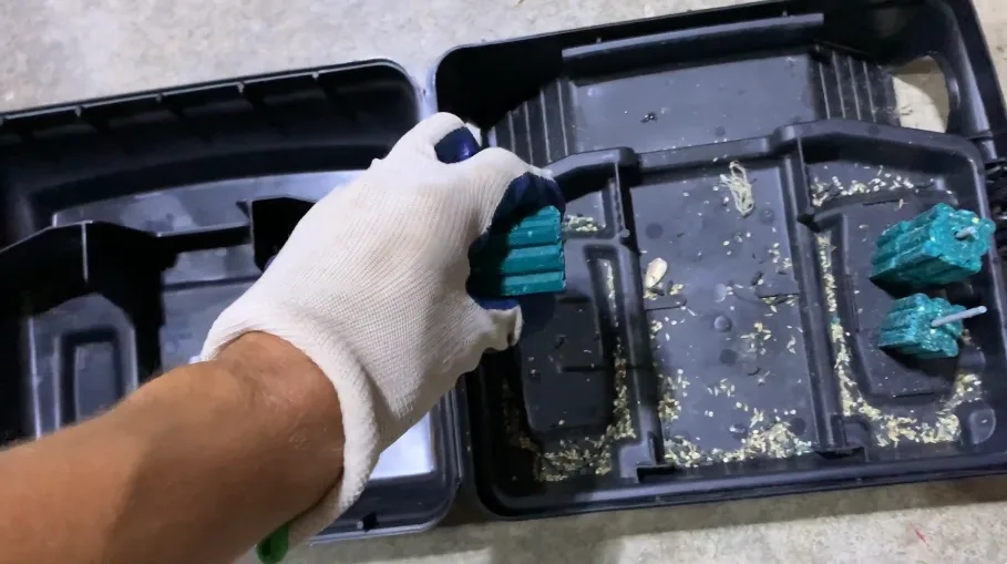 Gloved hand placing bait blocks into a station that shows rodent droppings inside