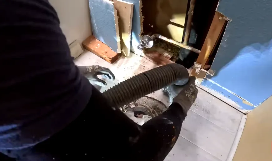 Flexible duct hose being fed through a wall opening during attic work