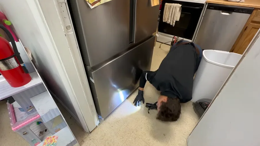 Technician on the floor with a light checking behind a commercial refrigerator