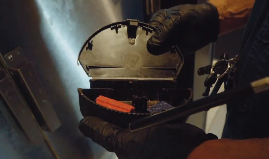 Gloved hand at an opened bait station holding a fresh bait block