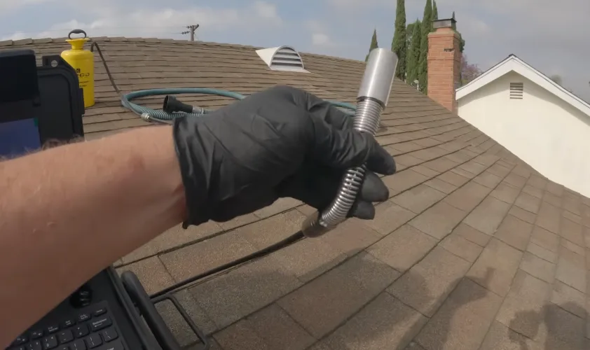 Gloved hand holding flexible duct against shingles while working on a roof penetration