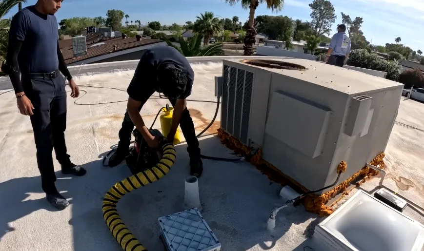 Crew working around a rooftop HVAC unit with a vacuum hose