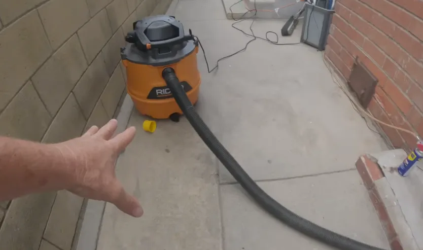 Shop vacuum hose run along a garage foundation edge during a cleanout