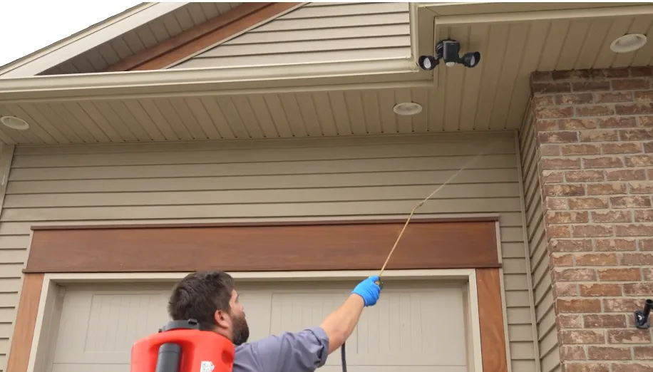 Technician directing a spray wand into the soffit above a garage door