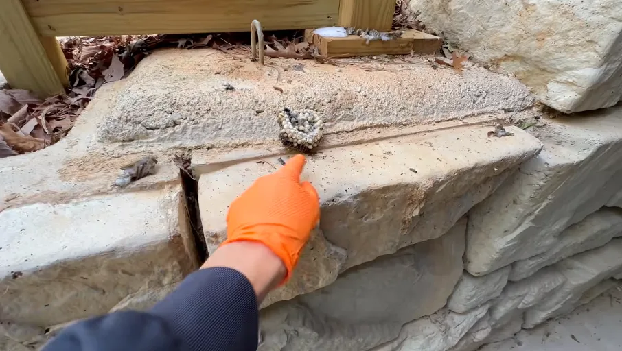 Gloved hand at a gap in a stone ledge where a weep hole opens into the wall