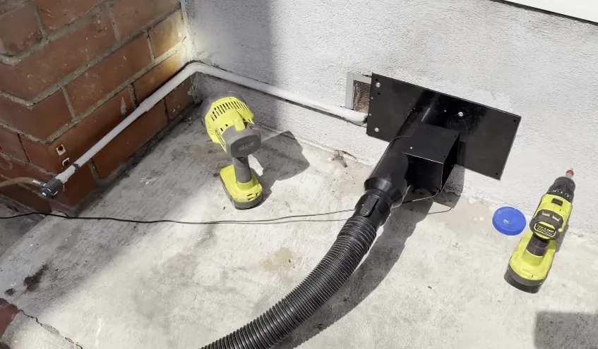 Vacuum hose and hand tool at a foundation crawl space opening