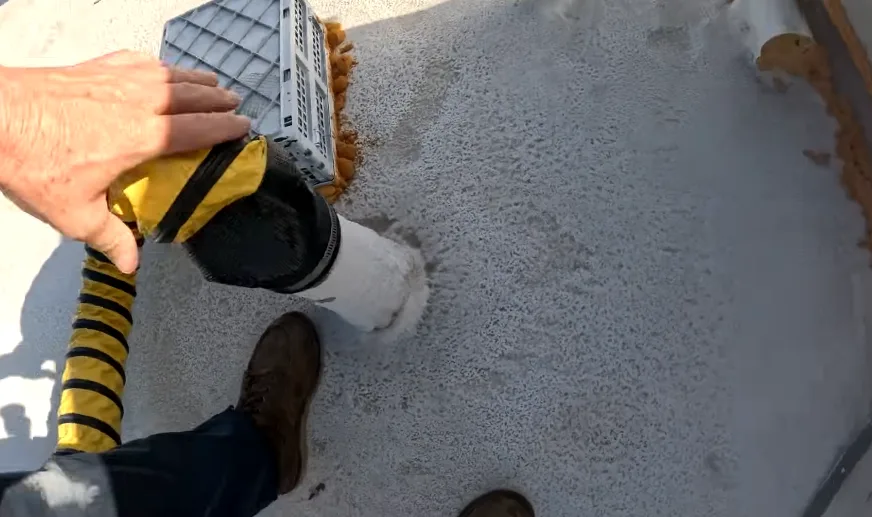 Vacuum hose held to a pipe penetration in a stucco wall to clear debris from the opening